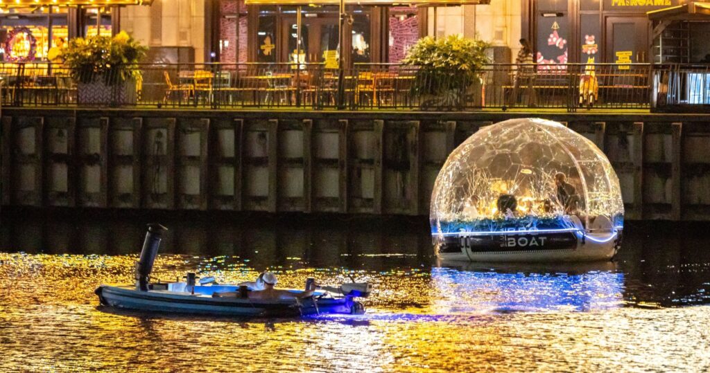 夜晚的 Canary Wharf，冰屋船行駛於水道間，璀璨燈光與水面倒影相映成趣。